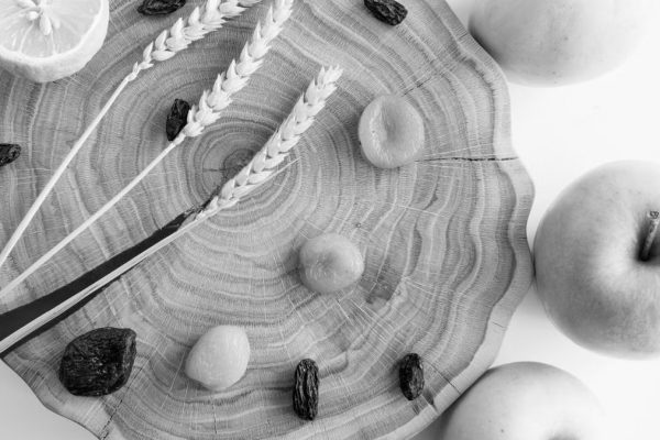 Elegant black and white still life featuring apples, lemon, wheat, and raisins on wood.