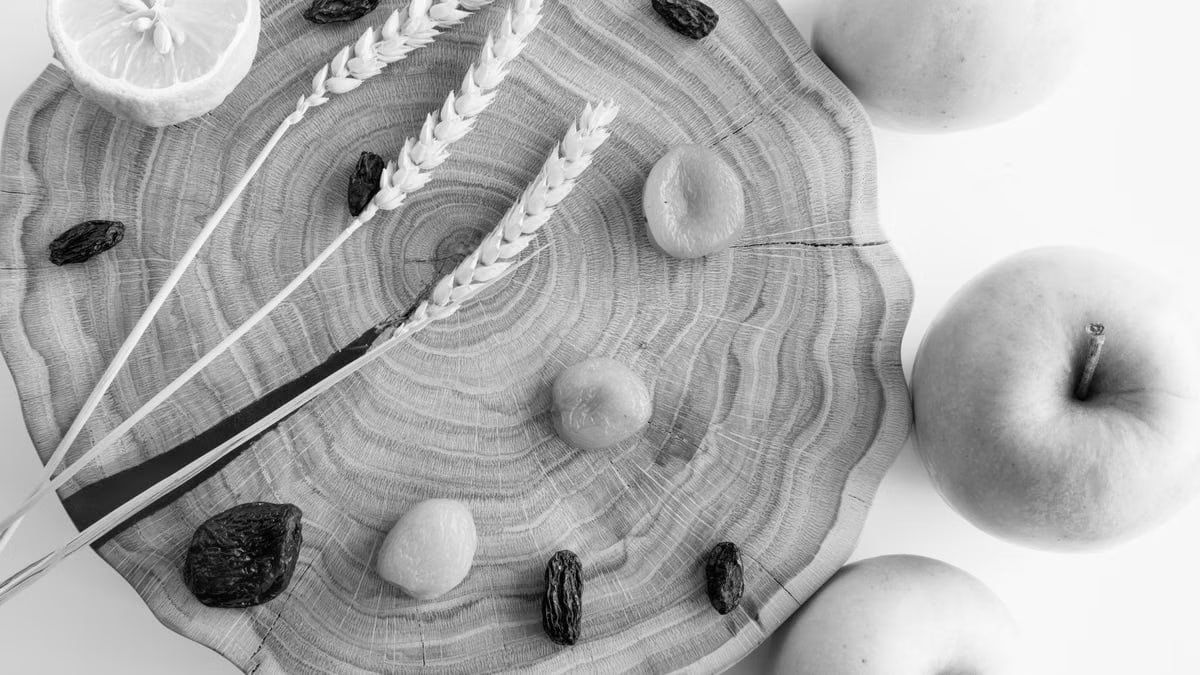 Elegant black and white still life featuring apples, lemon, wheat, and raisins on wood.